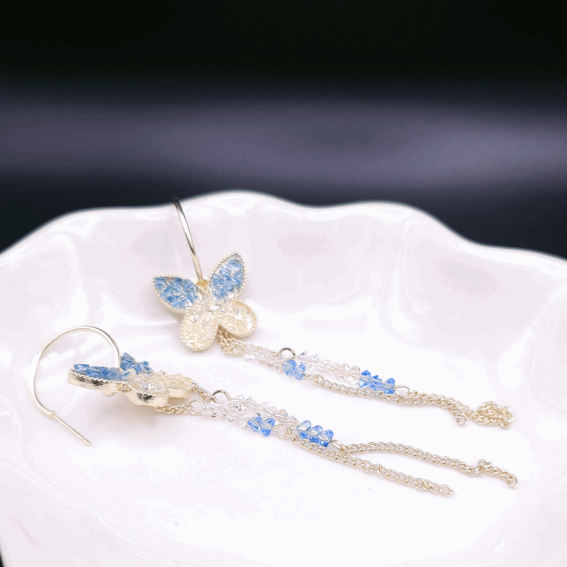 Close-up of Fairy-tale Earrings showcasing the intricate butterfly dangle design with blue and clear sparkles against a gold base.